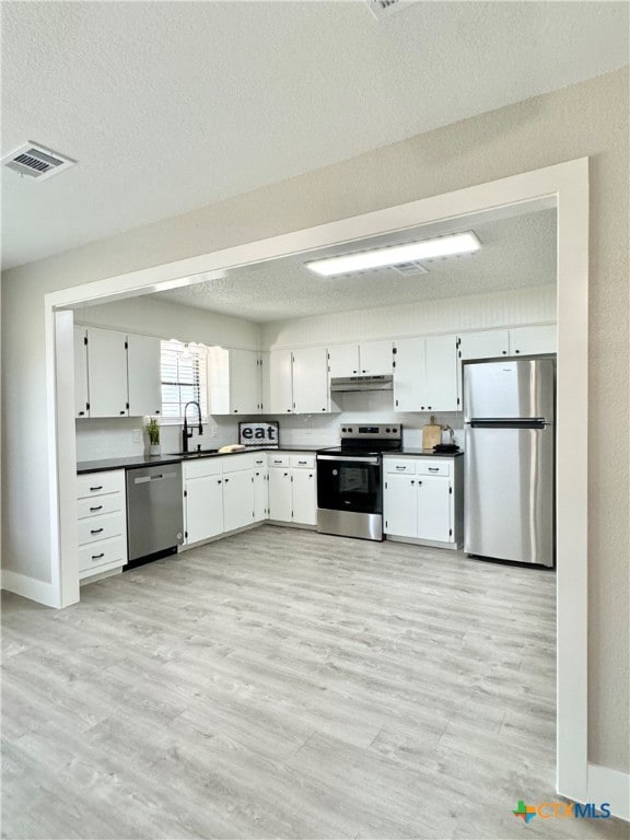 kitchen with stainless steel appliances, light hardwood / wood-style floors, white cabinets, and a textured ceiling