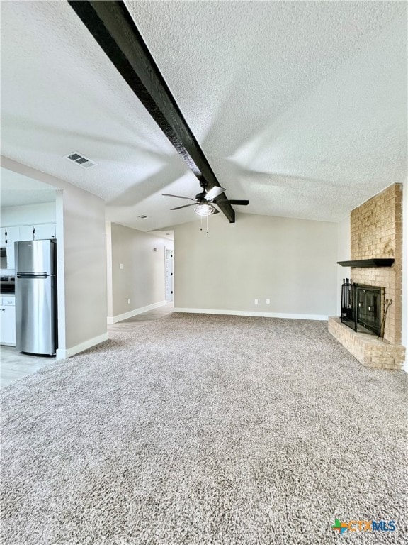 unfurnished living room with ceiling fan, a textured ceiling, beam ceiling, a brick fireplace, and carpet floors