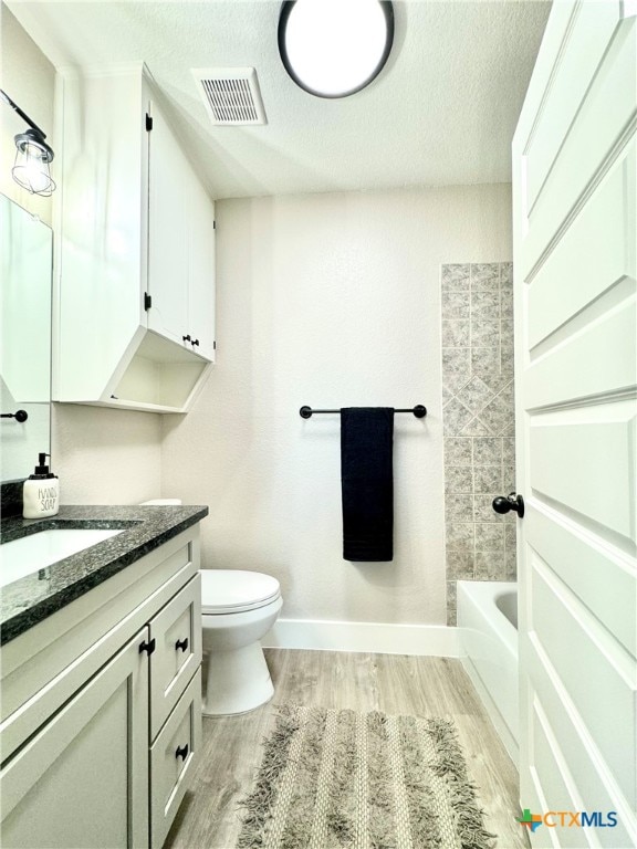 full bathroom with tiled shower / bath, a textured ceiling, wood-type flooring, vanity, and toilet