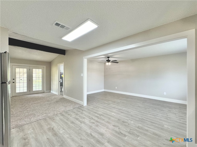 unfurnished room featuring ceiling fan, a textured ceiling, light hardwood / wood-style flooring, vaulted ceiling with beams, and french doors