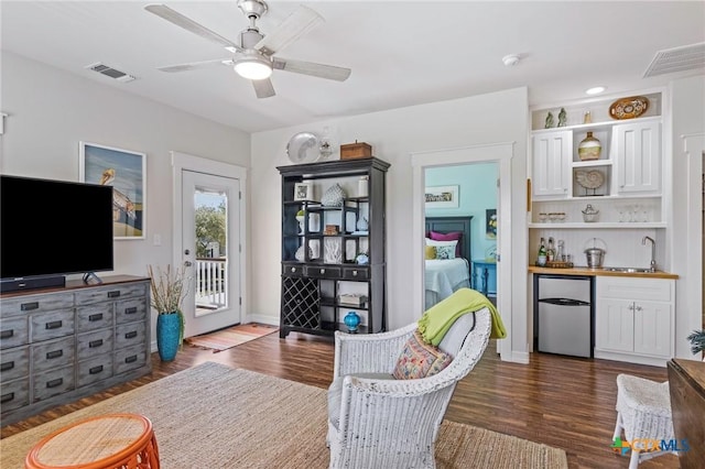 living room with ceiling fan, dark wood-style flooring, visible vents, and wet bar