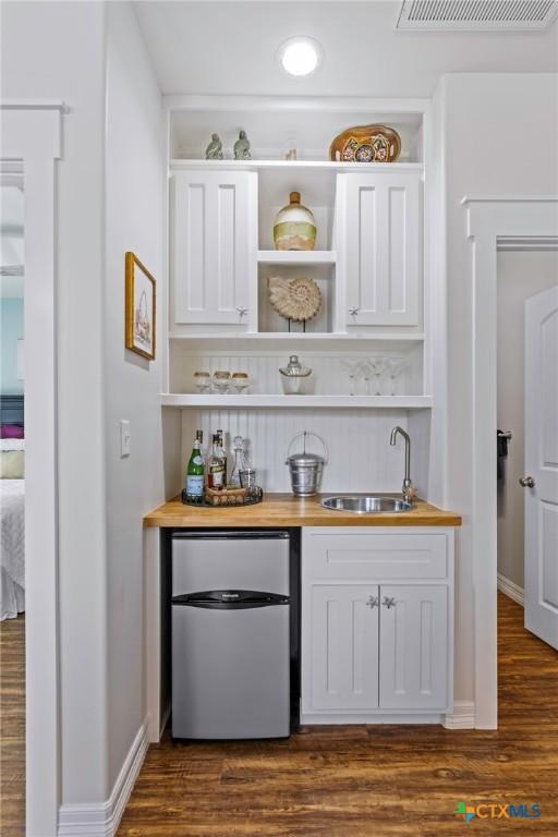 bar featuring refrigerator, dark wood finished floors, visible vents, and a sink