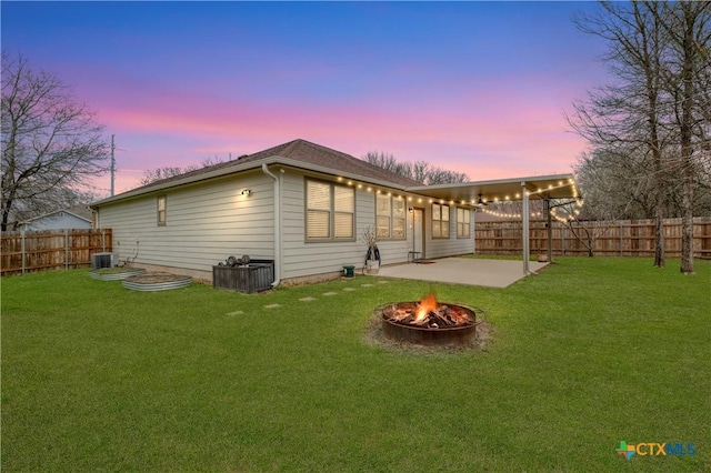 back house at dusk with a patio, a yard, central AC, and a fire pit