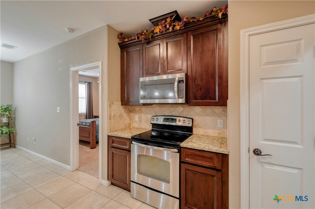 kitchen featuring appliances with stainless steel finishes, light stone countertops, light tile patterned floors, and backsplash