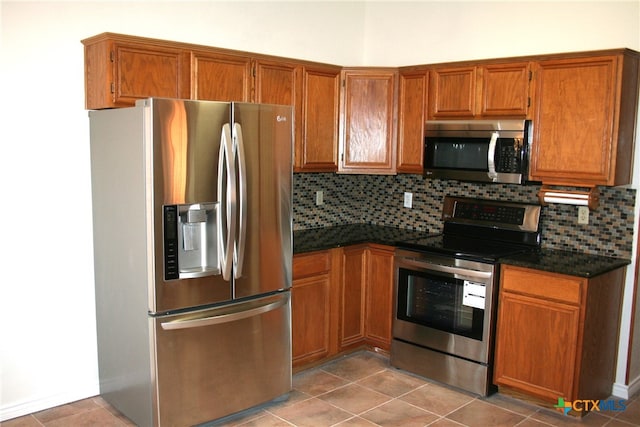 kitchen featuring light tile patterned floors, stainless steel appliances, dark stone counters, and tasteful backsplash