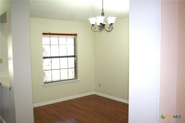 spare room with a notable chandelier and dark hardwood / wood-style floors