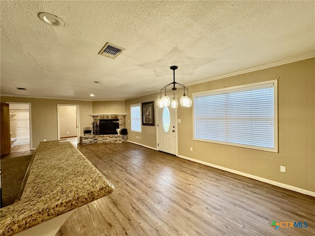 unfurnished living room with visible vents, crown molding, a stone fireplace, and wood finished floors