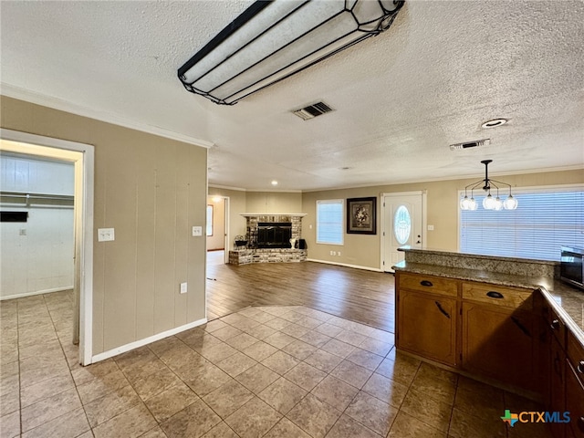 kitchen featuring dark countertops, visible vents, ornamental molding, and a stone fireplace