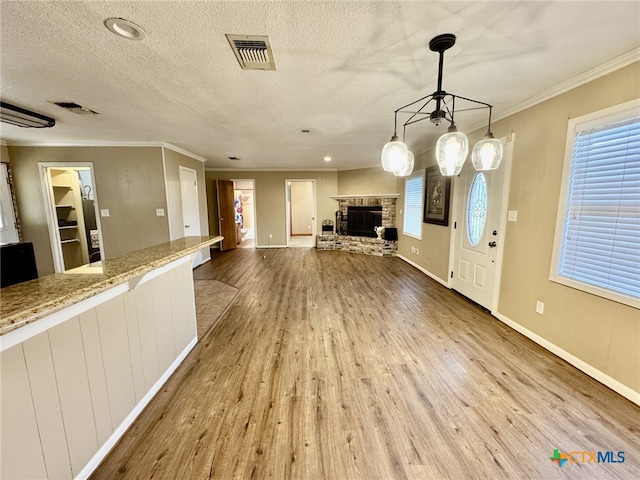 unfurnished living room featuring a stone fireplace, wood finished floors, visible vents, and crown molding