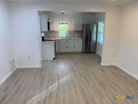 kitchen featuring stainless steel fridge, stove, tasteful backsplash, light hardwood / wood-style flooring, and hanging light fixtures