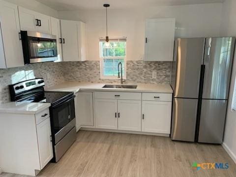 kitchen with appliances with stainless steel finishes, white cabinetry, hanging light fixtures, and sink