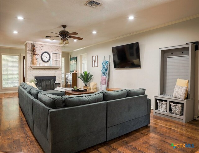 living room with ceiling fan, dark hardwood / wood-style floors, a large fireplace, and ornamental molding