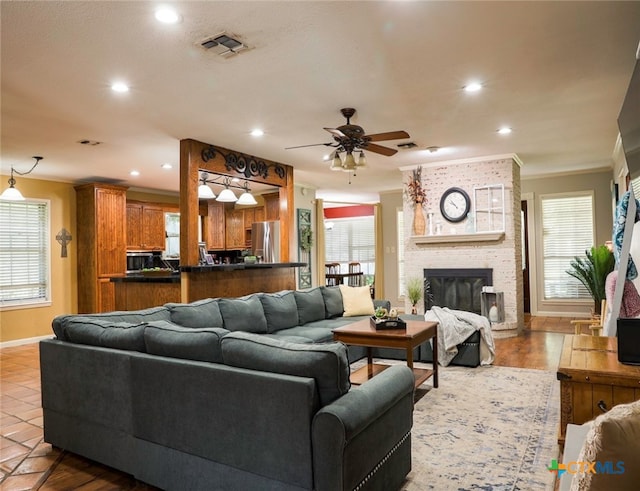 tiled living room featuring a fireplace, crown molding, ceiling fan, and plenty of natural light