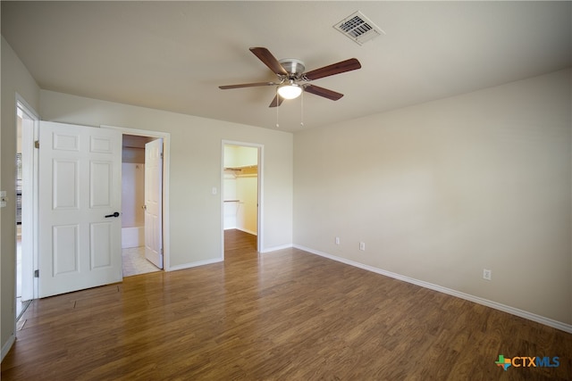 unfurnished bedroom featuring a closet, a walk in closet, hardwood / wood-style flooring, and ceiling fan