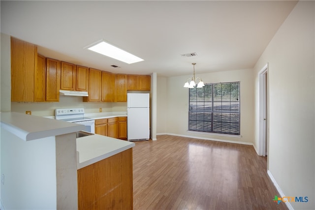 kitchen with kitchen peninsula, a notable chandelier, pendant lighting, light hardwood / wood-style flooring, and white appliances