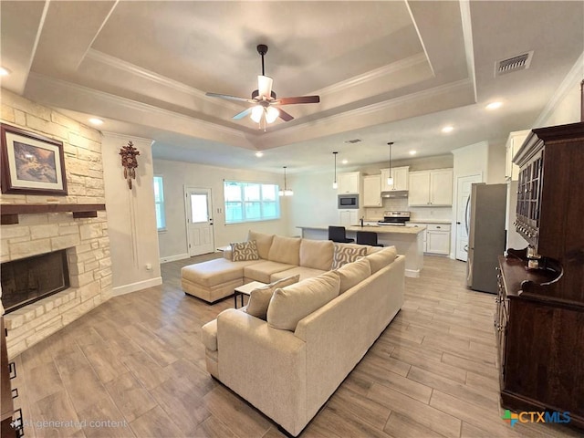 2635 Belle Hubbard Trl, Belton, TX 76513 - living room with a tray ceiling, a ceiling fan, light wood-style floors, a fireplace, and ornamental molding