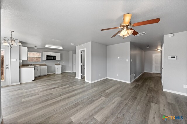 unfurnished living room with a textured ceiling, sink, wood-type flooring, and ceiling fan with notable chandelier