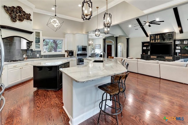 kitchen featuring high vaulted ceiling, a large island with sink, a breakfast bar area, arched walkways, and appliances with stainless steel finishes