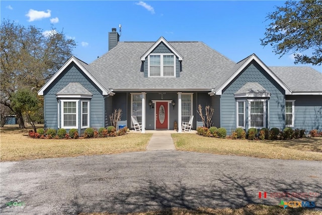 view of front facade featuring a porch, a chimney, a front yard, and a shingled roof