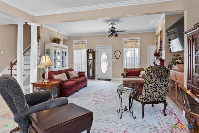 living room featuring a ceiling fan, crown molding, baseboards, stairs, and ornate columns