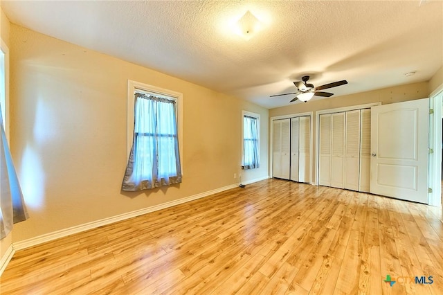 unfurnished bedroom featuring ceiling fan, a textured ceiling, light hardwood / wood-style flooring, and multiple closets