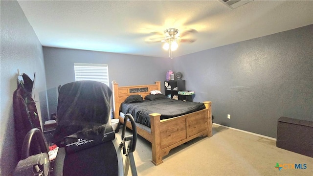 bedroom featuring a textured wall, light colored carpet, visible vents, baseboards, and a ceiling fan