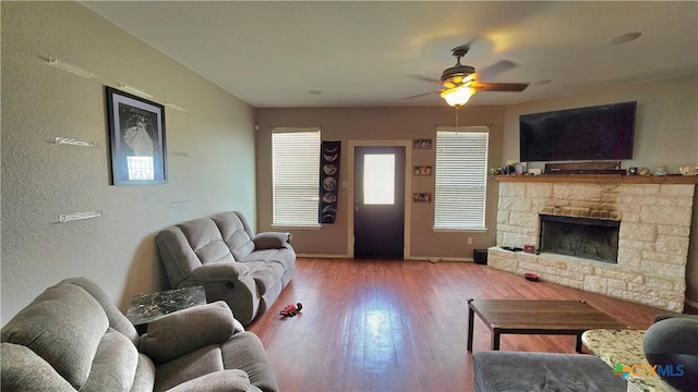 living area with a ceiling fan, a fireplace, baseboards, and wood finished floors