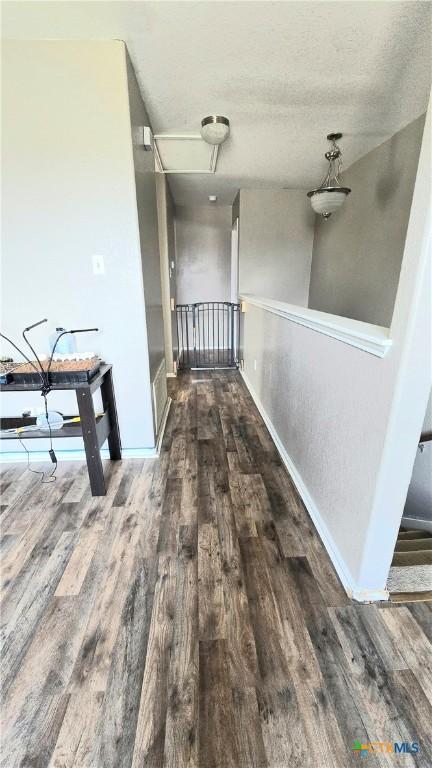 corridor featuring a textured ceiling, baseboards, wood finished floors, and an upstairs landing