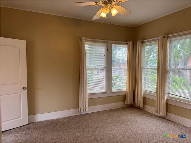 empty room featuring light colored carpet, a ceiling fan, and baseboards