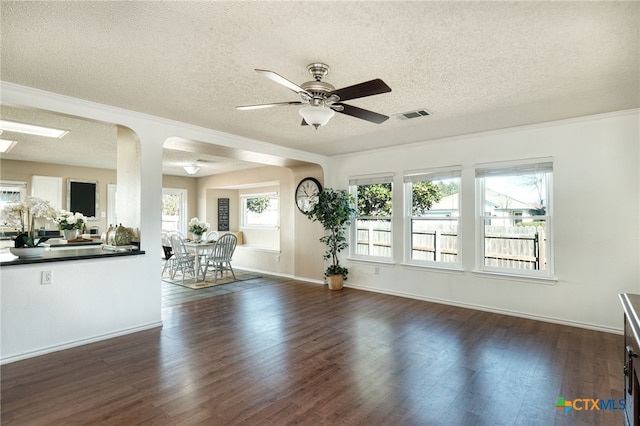 unfurnished living room with ceiling fan, ornamental molding, a textured ceiling, and dark wood-type flooring