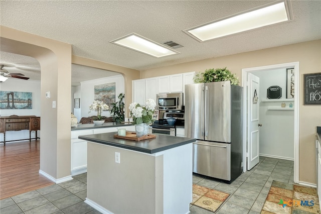 kitchen with a textured ceiling, stainless steel appliances, ceiling fan, light hardwood / wood-style flooring, and white cabinets