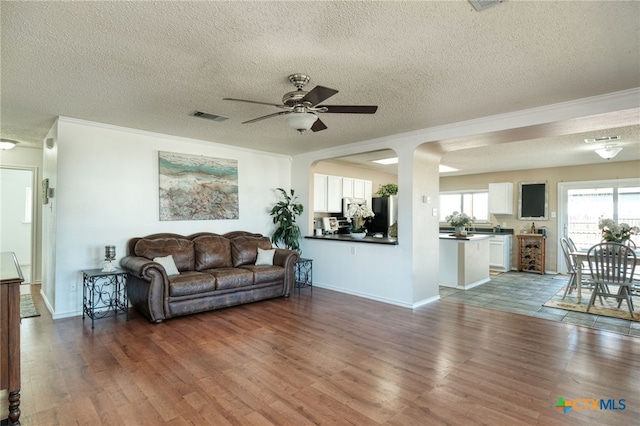 living room featuring ceiling fan, crown molding, dark wood-type flooring, and a textured ceiling