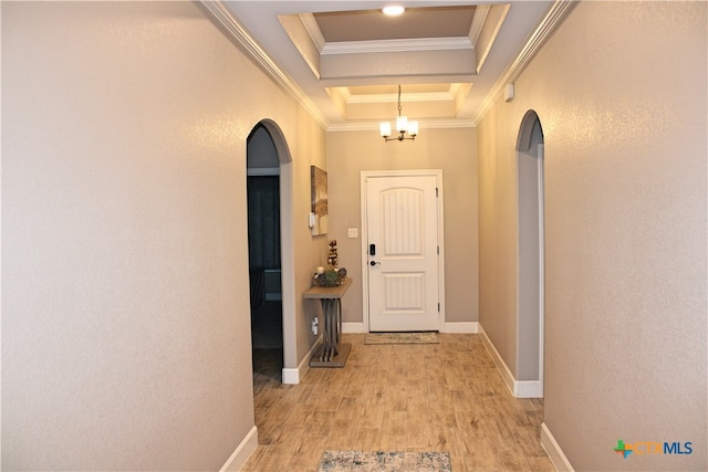 hallway with light hardwood / wood-style flooring, crown molding, an inviting chandelier, and a tray ceiling