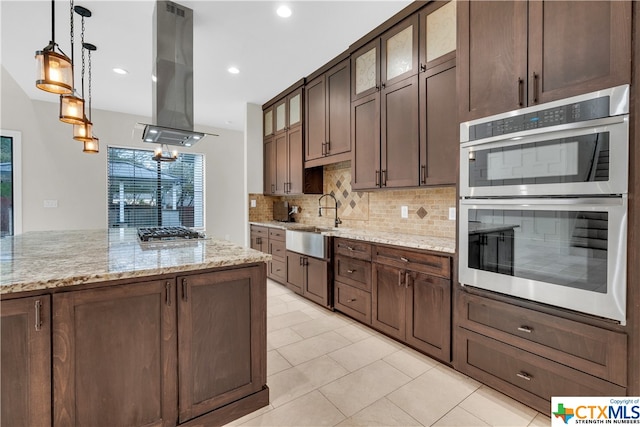 kitchen with island exhaust hood, stainless steel appliances, backsplash, light stone countertops, and sink