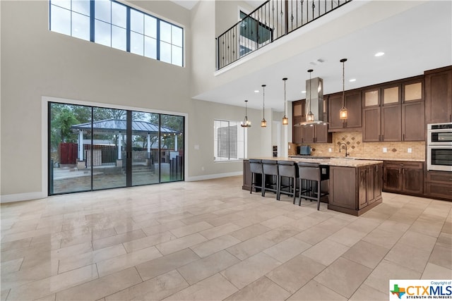 kitchen with a kitchen island with sink, a kitchen breakfast bar, exhaust hood, double oven, and decorative light fixtures