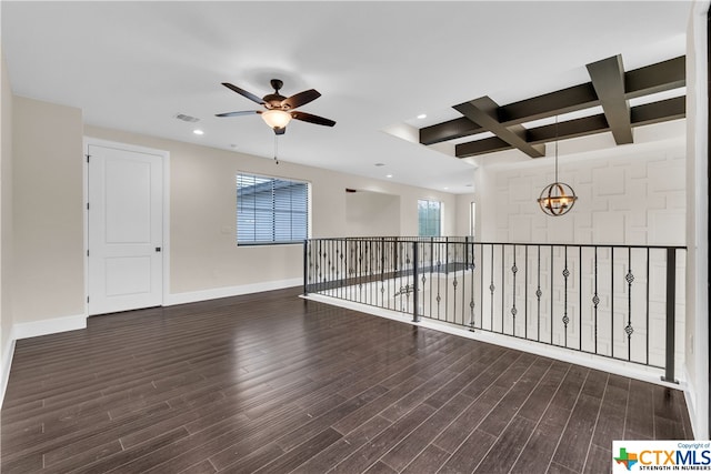 empty room with dark wood-type flooring, beamed ceiling, coffered ceiling, and ceiling fan with notable chandelier