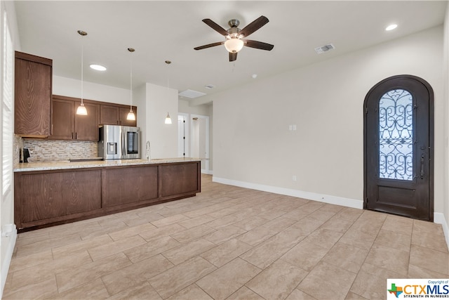 kitchen with light stone countertops, ceiling fan, backsplash, hanging light fixtures, and stainless steel fridge with ice dispenser