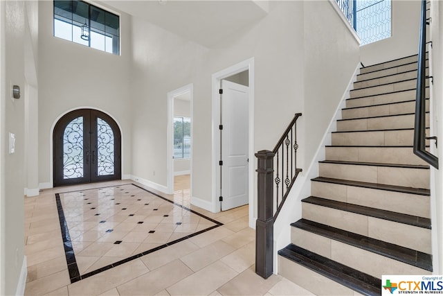 entrance foyer featuring a towering ceiling, light tile patterned floors, and french doors