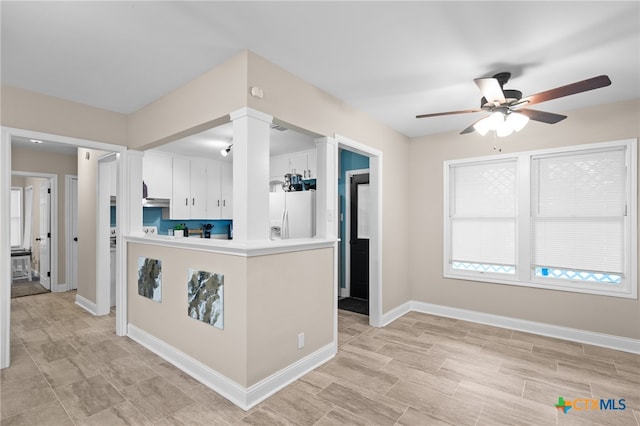 kitchen with ornate columns, white cabinetry, white refrigerator with ice dispenser, ceiling fan, and kitchen peninsula