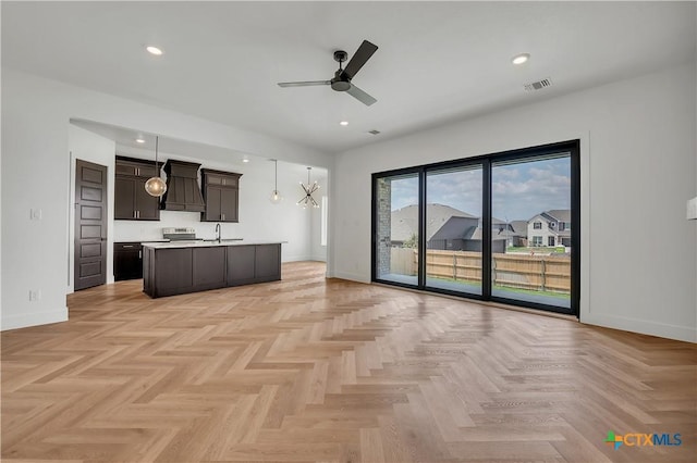 kitchen featuring decorative light fixtures, an island with sink, dark brown cabinetry, ceiling fan, and electric stove