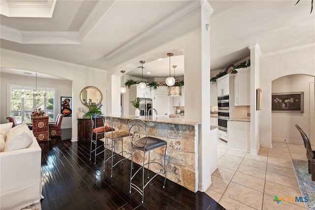 kitchen with white cabinets, appliances with stainless steel finishes, a kitchen breakfast bar, ornamental molding, and light wood-type flooring