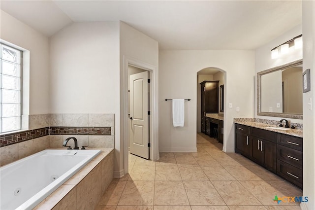 bathroom featuring lofted ceiling, tile patterned flooring, vanity, baseboards, and a tub with jets