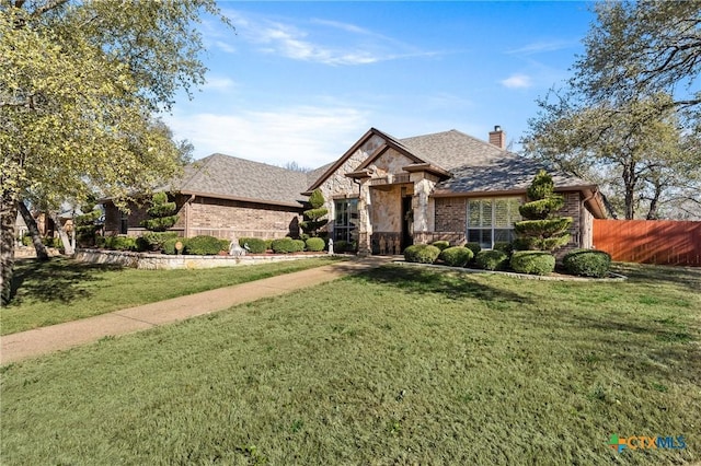 french provincial home with brick siding, fence, stone siding, a front lawn, and a chimney