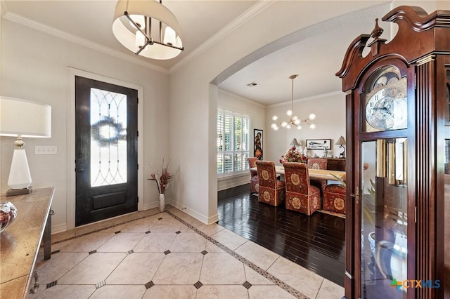 entryway featuring arched walkways, ornamental molding, an inviting chandelier, and baseboards