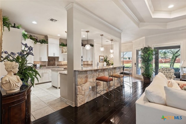 kitchen featuring a breakfast bar, a raised ceiling, visible vents, backsplash, and ornamental molding