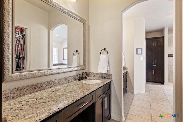 full bath with tile patterned flooring, a walk in closet, vanity, and baseboards