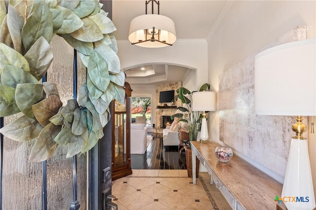 tiled foyer with arched walkways, a tray ceiling, ornamental molding, and a fireplace