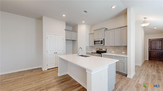 kitchen featuring sink, gray cabinets, decorative backsplash, a center island with sink, and appliances with stainless steel finishes