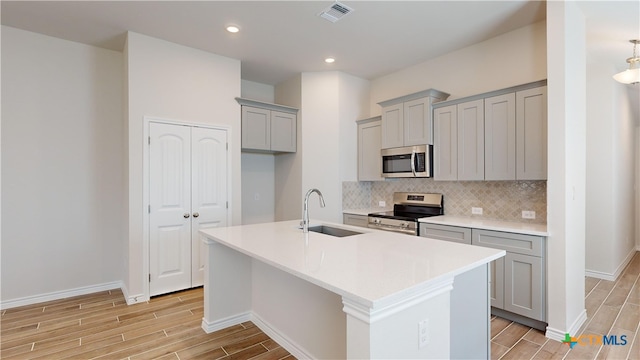 kitchen featuring tasteful backsplash, gray cabinetry, stainless steel appliances, a kitchen island with sink, and sink