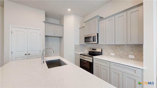 kitchen with gray cabinetry, decorative backsplash, sink, and appliances with stainless steel finishes